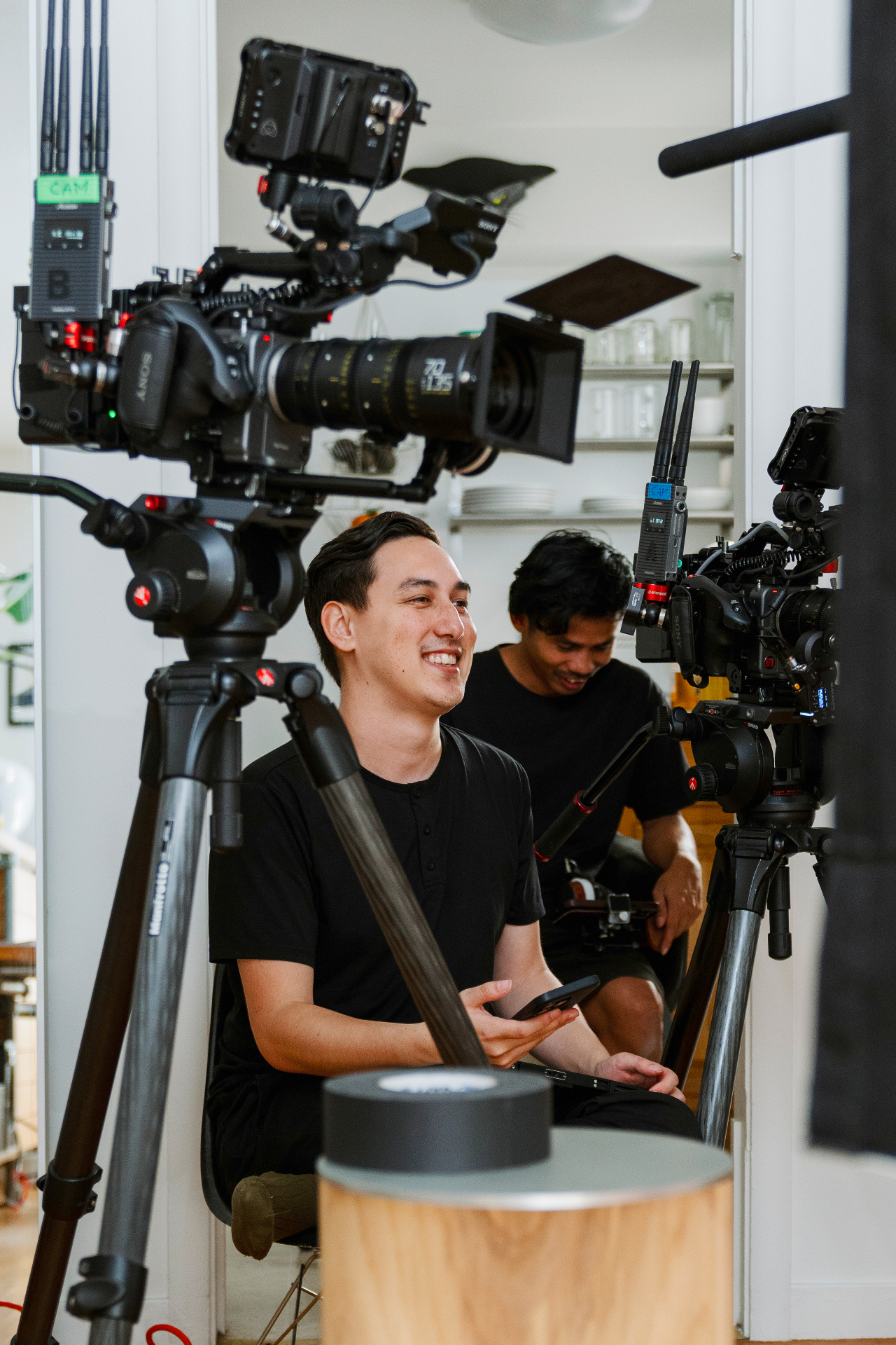 Leomar Moring smiling behind a pair of cinema cameras on set, in conversation with a collaborator.