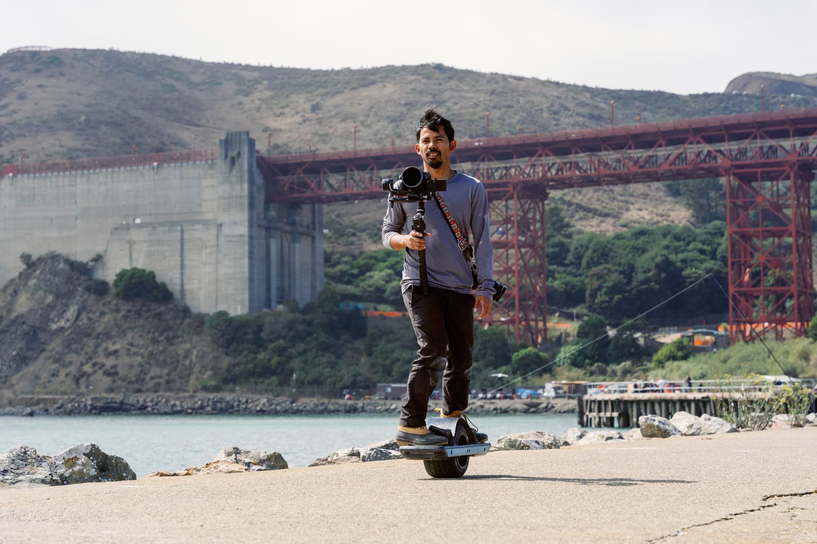 Videographer riding a Onewheel with a gimbal-mounted camera below the Golden Gate Bridge