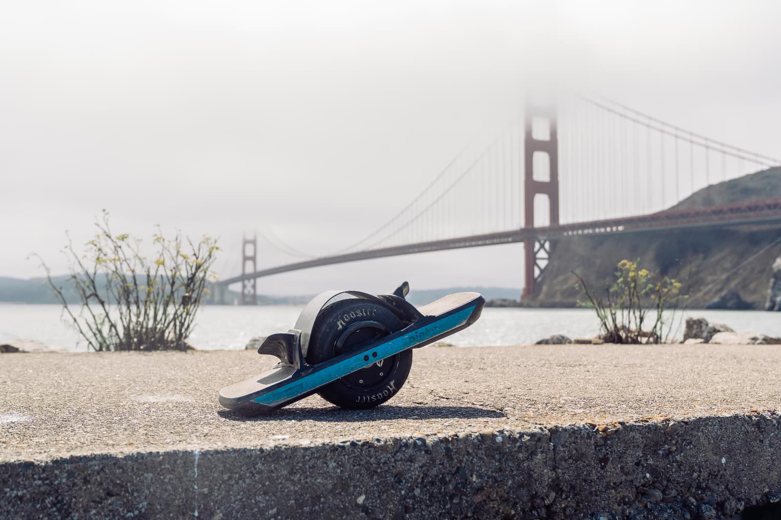 A Onewheel resting on a sea wall with the fog-covered Golden Gate Bridge behind it