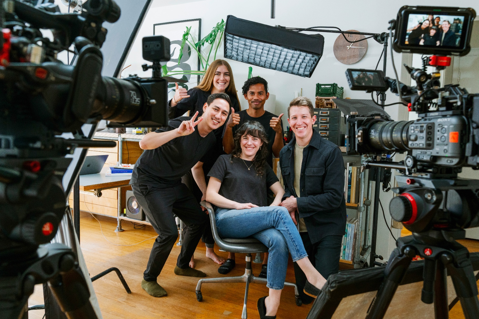 A five-person production crew smiling and posing together between two cinema camera rigs in a studio.