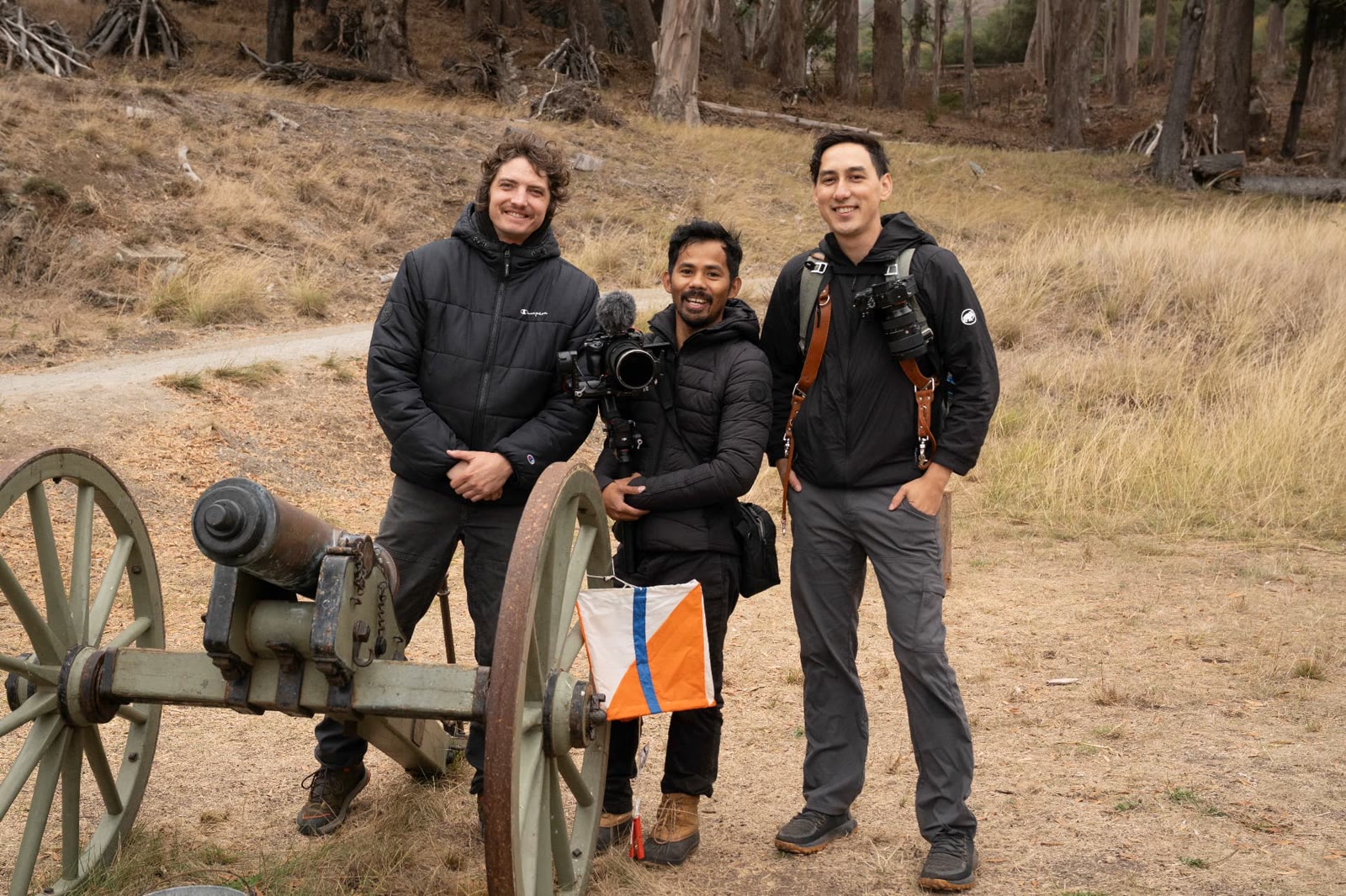 Three members of the media crew standing beside the cannon on Angel Island, holding camera gear